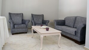 A room with two grey armchairs, a grey sofa, and a white coffee table with a decorative item. - Ataol Otel (Bozcaada)