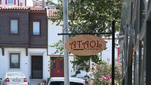 A street view with a sign for a restaurant, parked cars, and potted plants along the sidewalk. - Ataol Otel (Bozcaada)