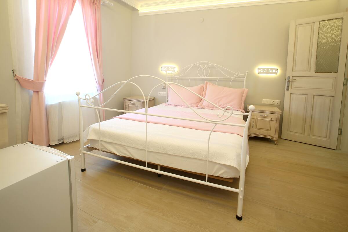 A bedroom with a white metal bed frame, a bedside table, a nightstand, and a door with a frosted glass panel.
