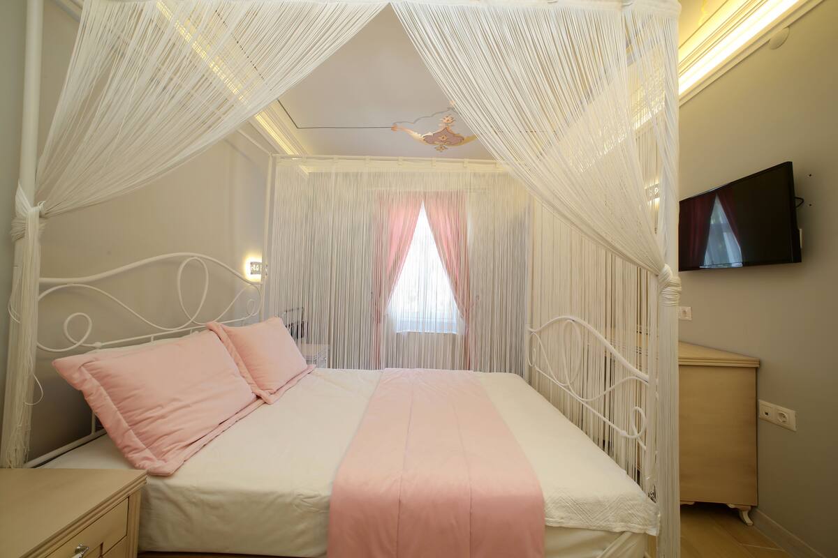 A bedroom with a bed, curtains, a television, and a bedside table.