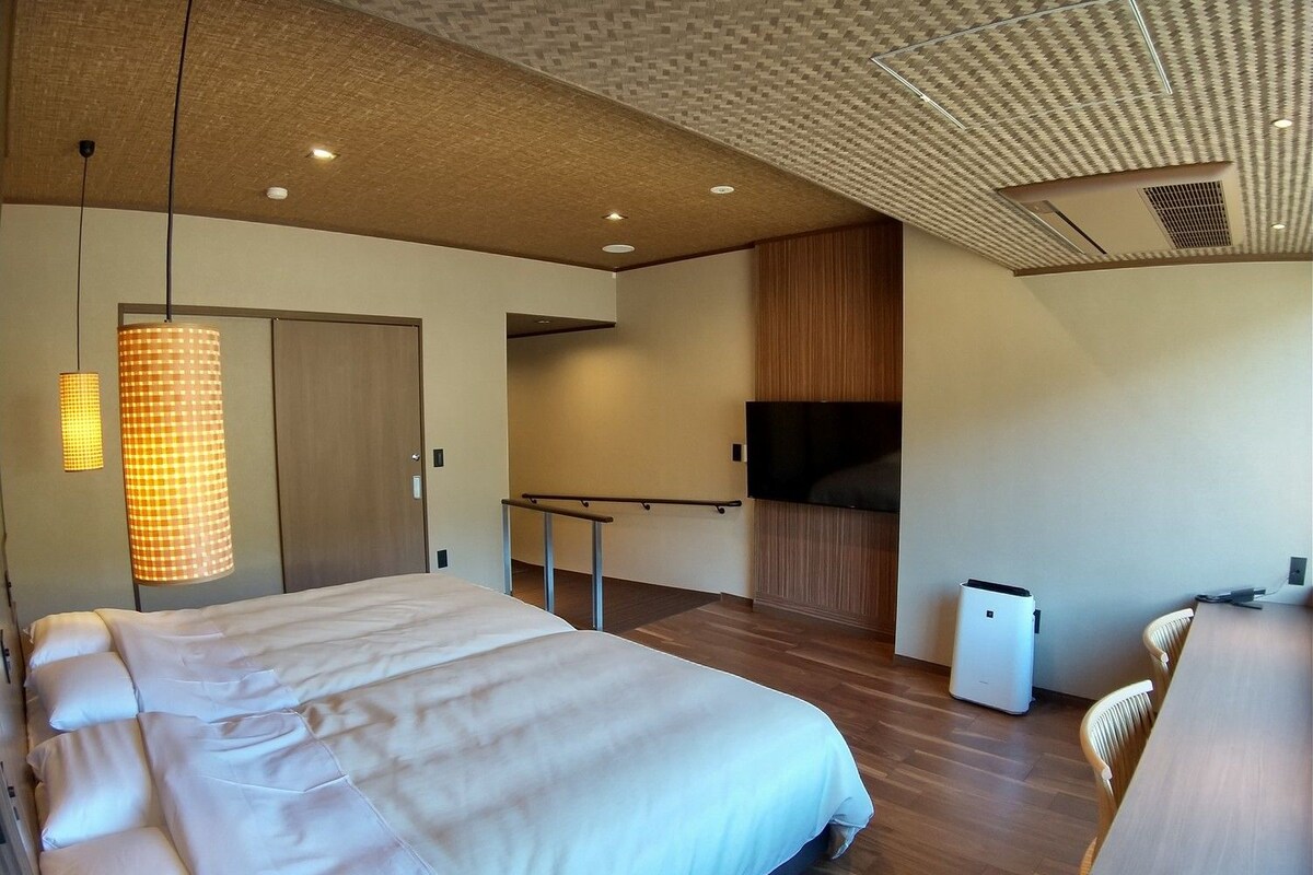A modern hotel room with a large bed, a TV, a desk, and a chair.