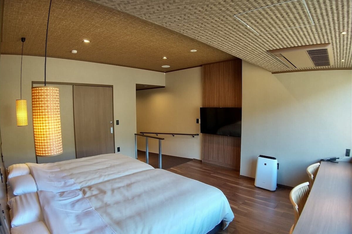 A modern hotel room with a large bed, a TV, a desk, and a chair.