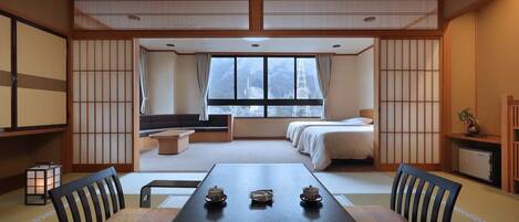 A traditional Japanese room with tatami flooring, a low table with tea sets, a futon bed, and a view of a mountain.