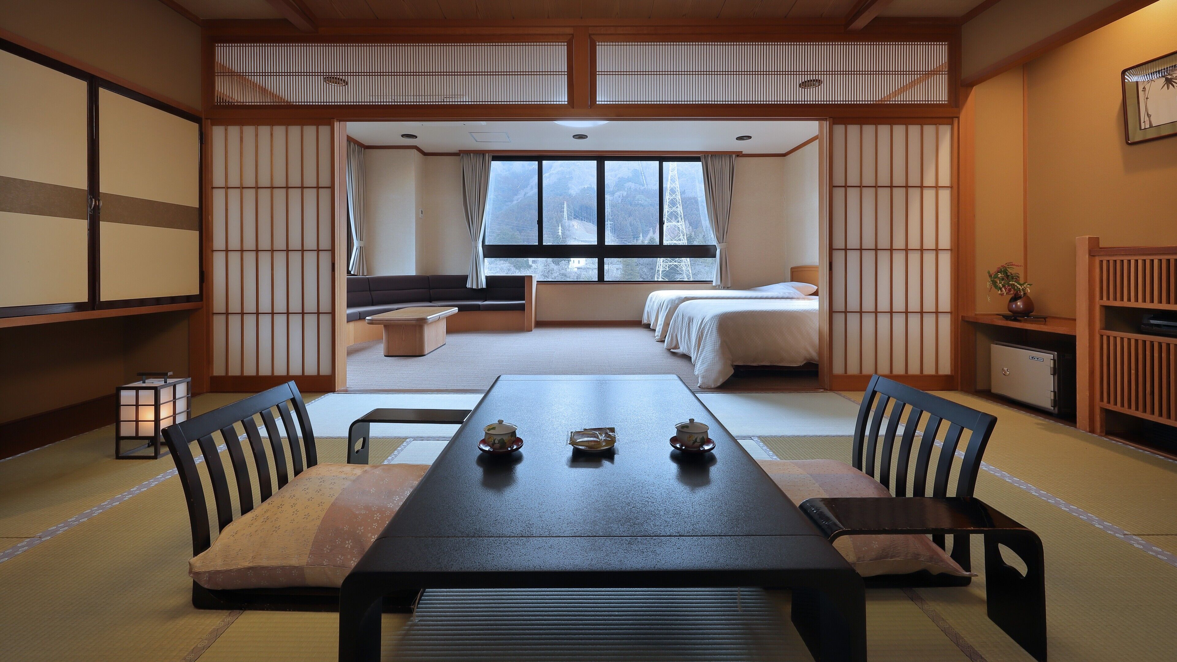 Ein traditioneller japanischer Raum mit Tatami-Boden, einem niedrigen Tisch mit Teesets, einer Couch und einem Bett mit weißer Bettwäsche.