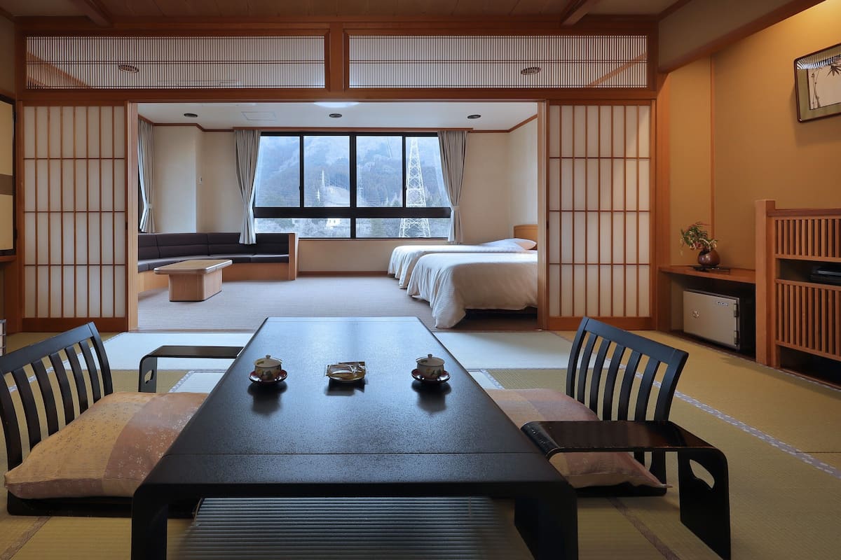 A traditional Japanese room with tatami flooring, a low table with tea sets, a sofa, and a bed with white bedding.
