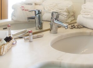 A bathroom sink with two chrome faucets, a mirror, and neatly folded white towels. - Hotel Michela (Male)