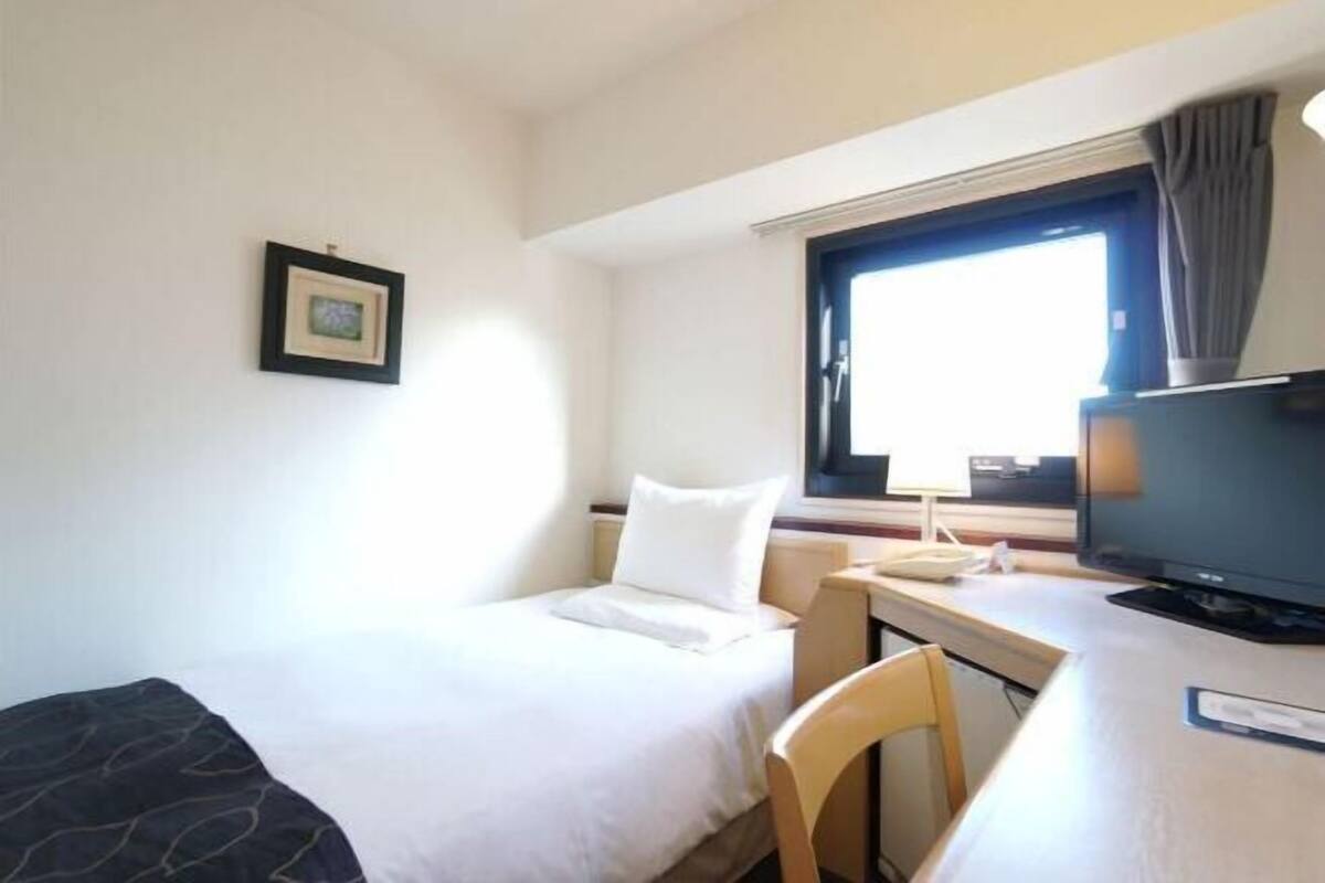 Une chambre d’hôtel équipée d’un lit, d’un bureau, d’une chaise, d’une télévision et d’une fenêtre avec des rideaux.