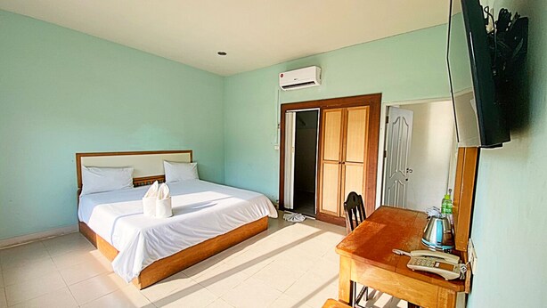 A hotel room with a bed, a desk, a chair, a TV, and an air conditioning unit. - OK Hotel (Chumphon)