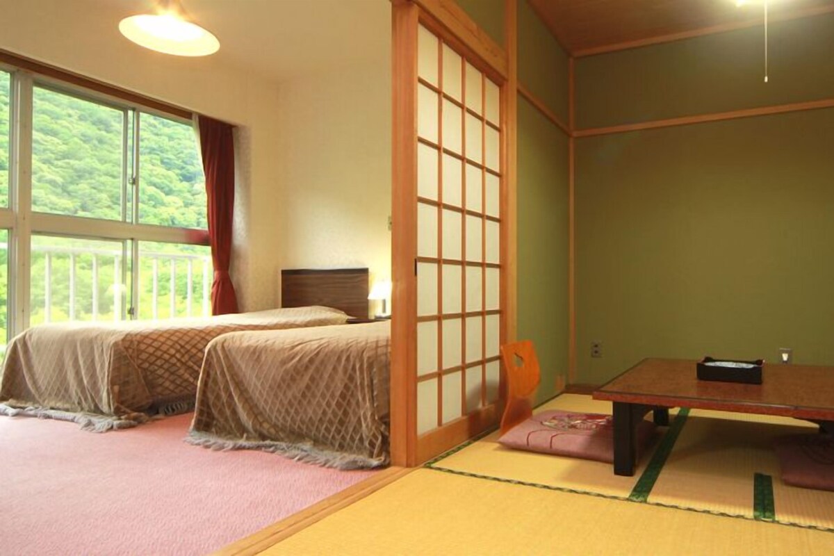 Ein traditioneller japanischer Raum mit Tatami-Bodenbelag, einem niedrigen Tisch und zwei Betten.