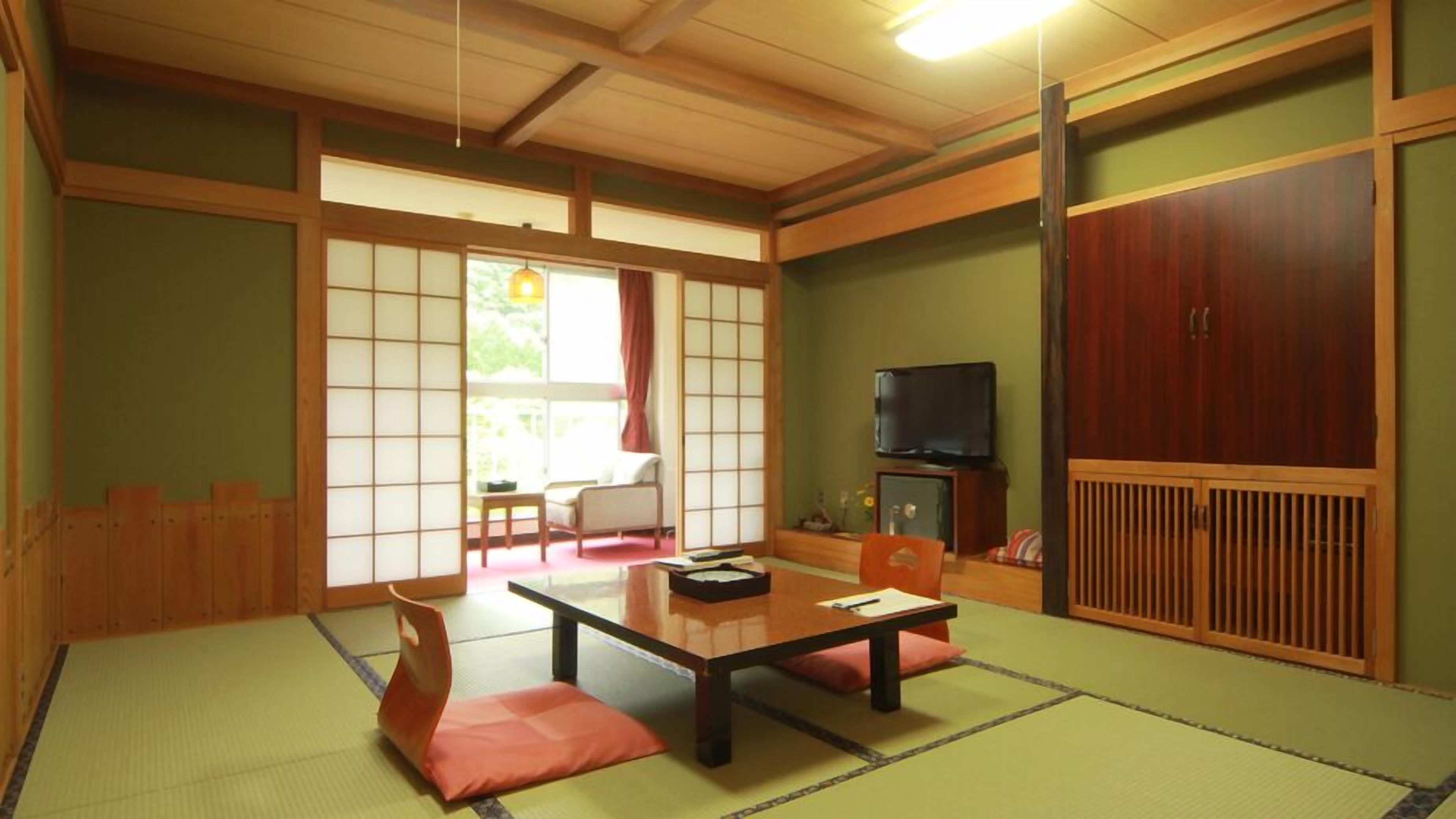A traditional Japanese room with tatami flooring, a low table, cushions, sliding doors, and a television.