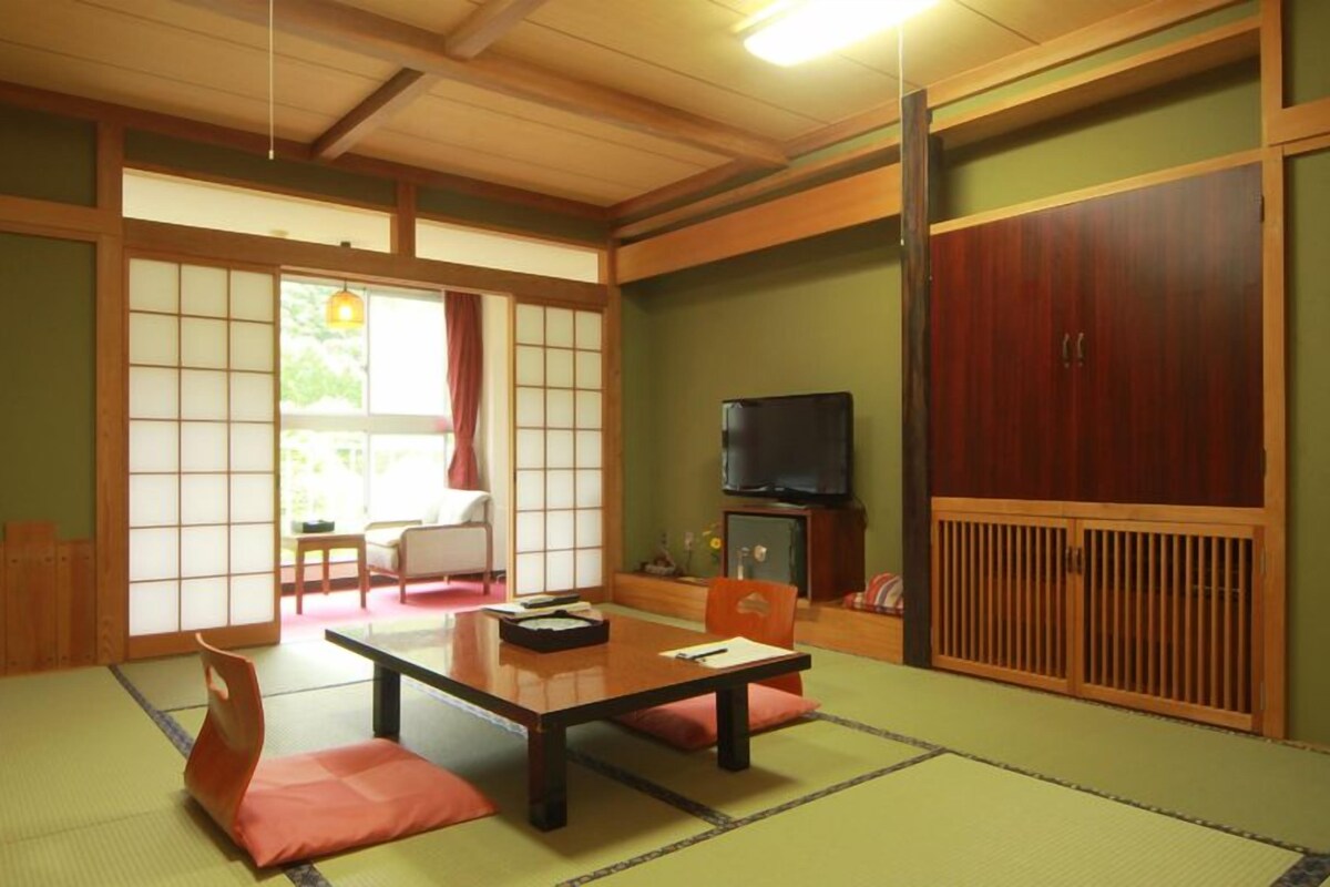 Una habitación japonesa tradicional con suelo de tatami, una mesa baja, cojines, puertas correderas y un televisor.