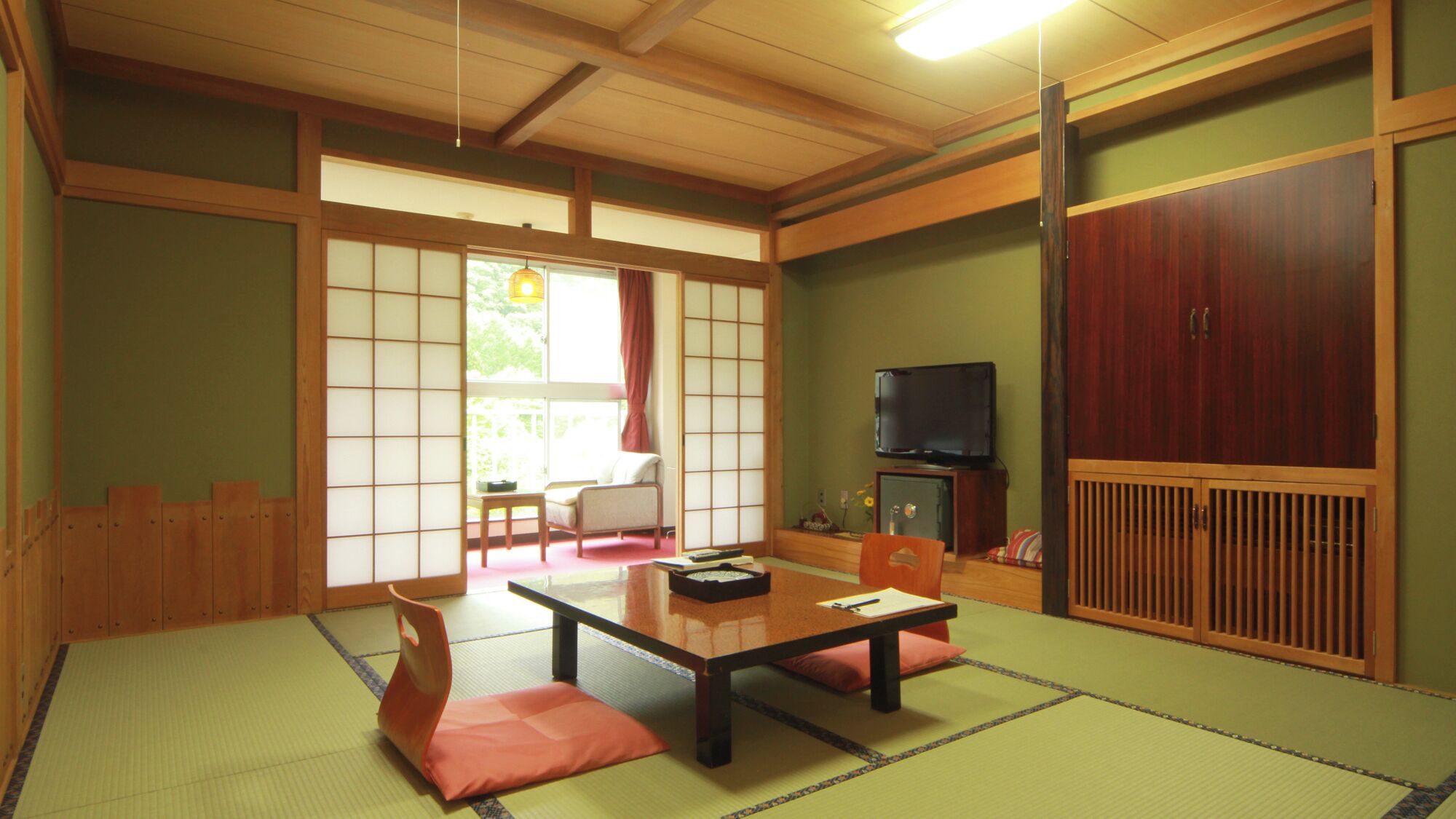 A traditional Japanese room with tatami flooring, a low table, cushions, sliding doors, and a television.