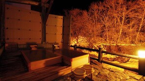 A wooden deck with hot tubs and stone seating, a wooden fence, and a view of a forested area at night. - Yunishigawa Hakuun-no-yado Yamashiroya (Nikko)