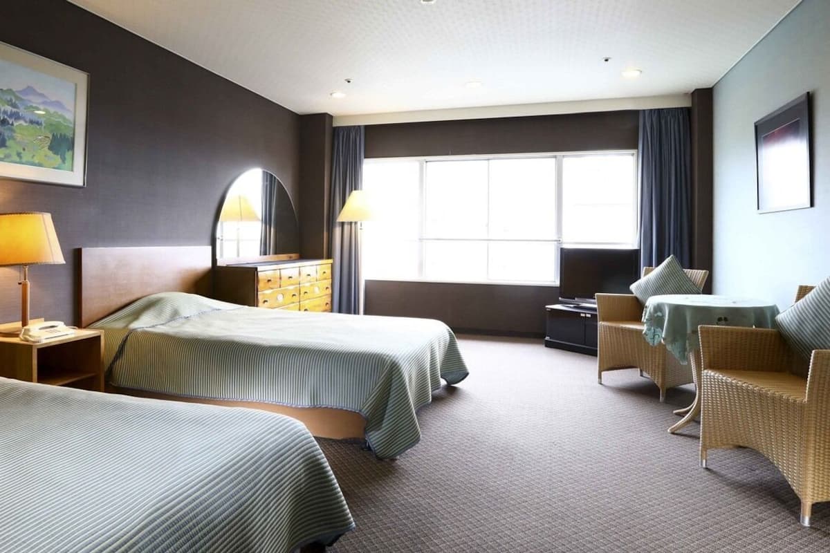 A hotel room with two beds, a desk, a chair, a lamp, a dresser, and a window.