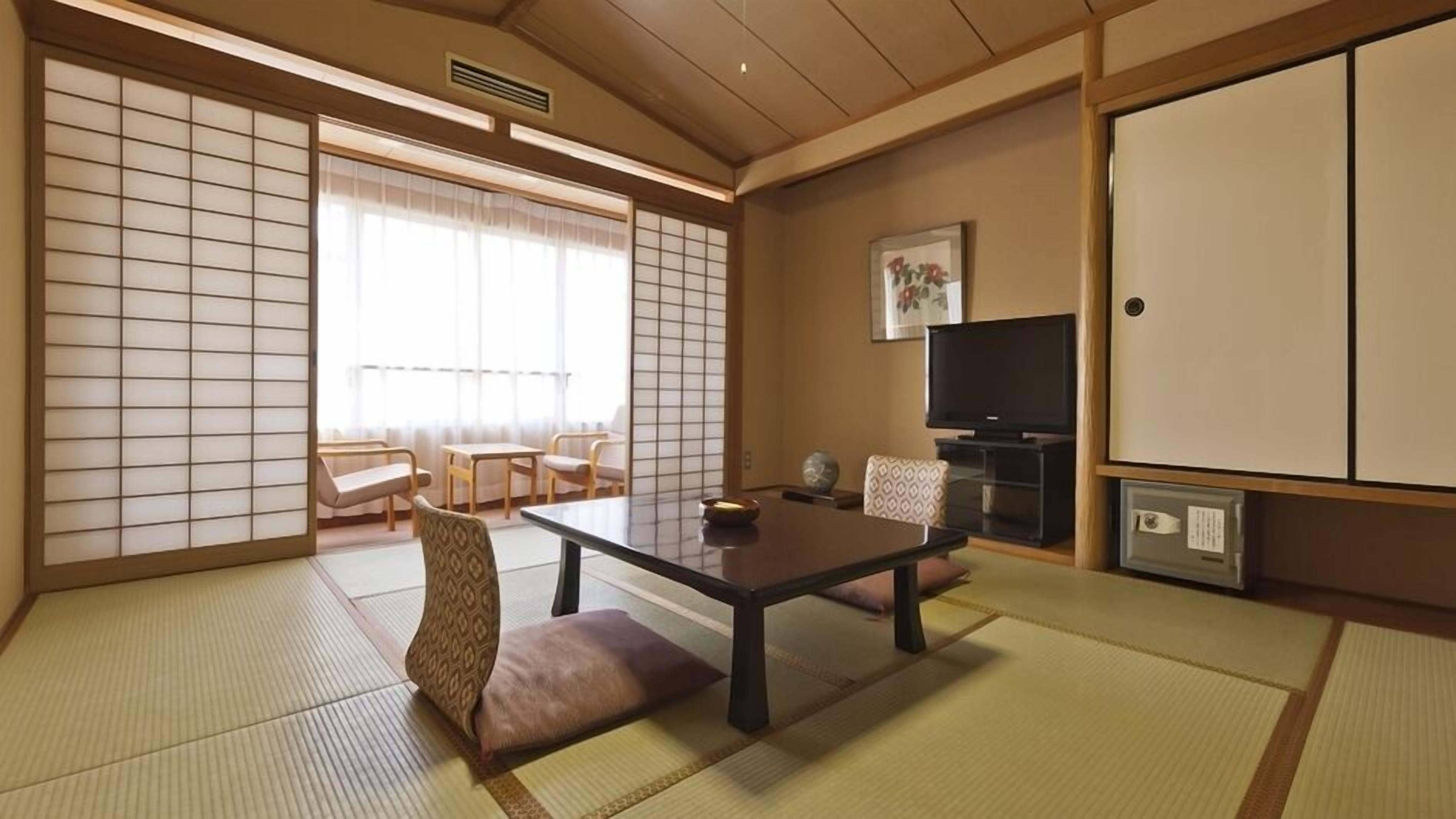 A traditional Japanese room with tatami flooring, a low table, seating, a television, and sliding doors.