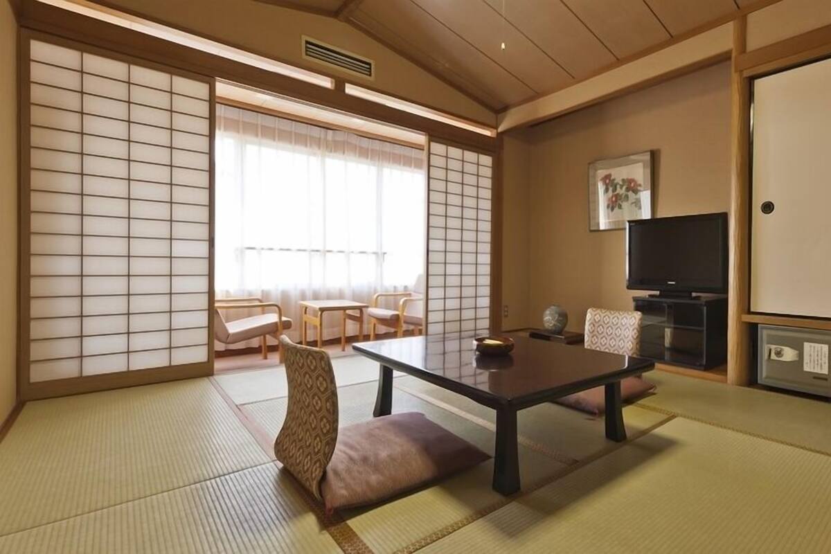 A traditional Japanese room with tatami flooring, a low table, seating, a television, and sliding doors.