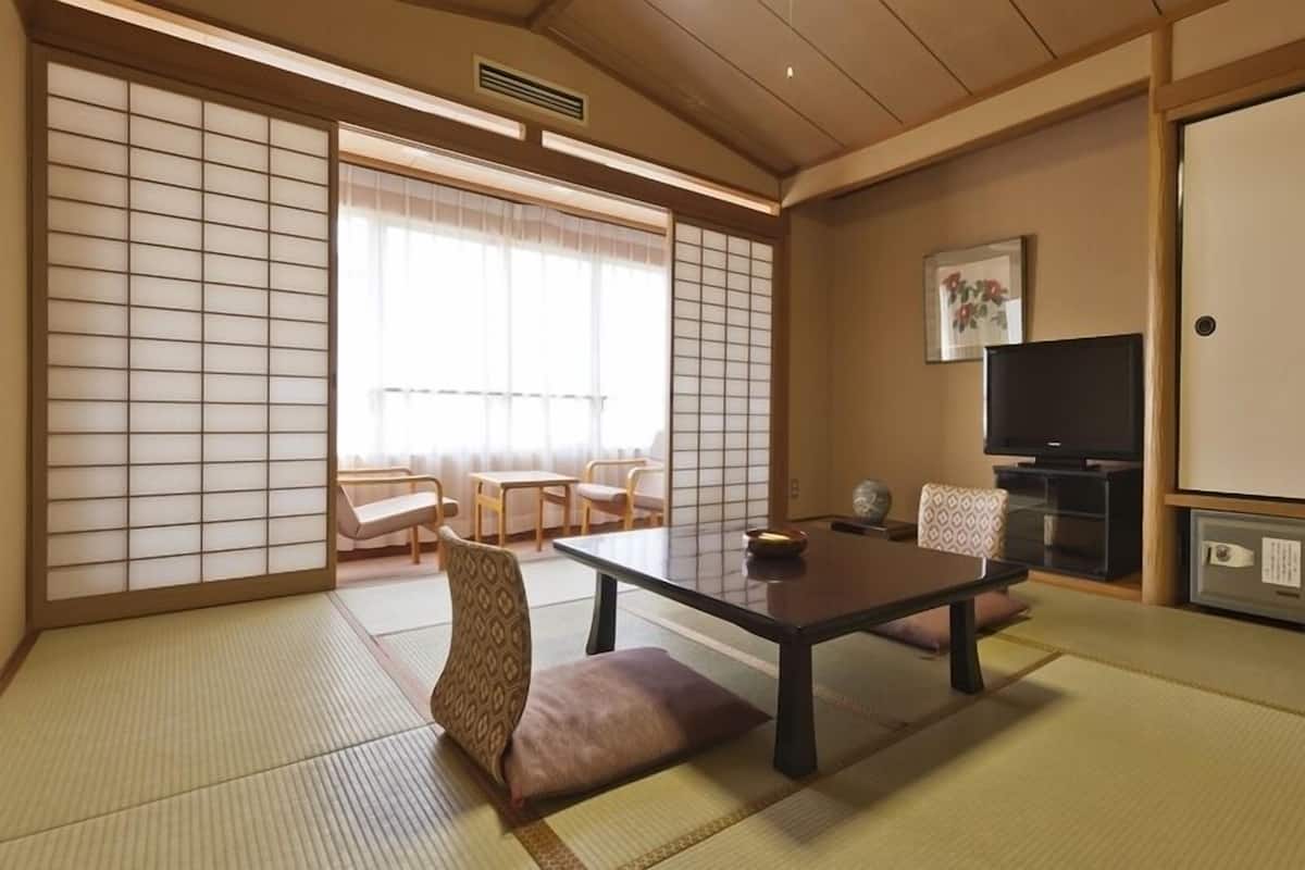 Une pièce de style japonais traditionnel, avec un sol recouvert de tatamis, une table basse, des sièges, un téléviseur et des portes coulissantes.