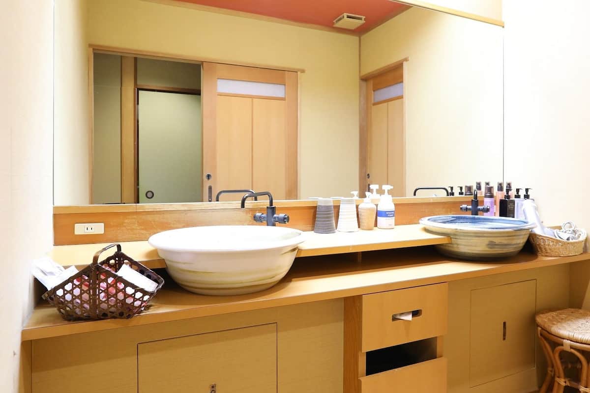 Une salle de bain avec un grand miroir, un meuble-lavabo en bois, un lavabo en forme de cuvette et un tabouret en osier.