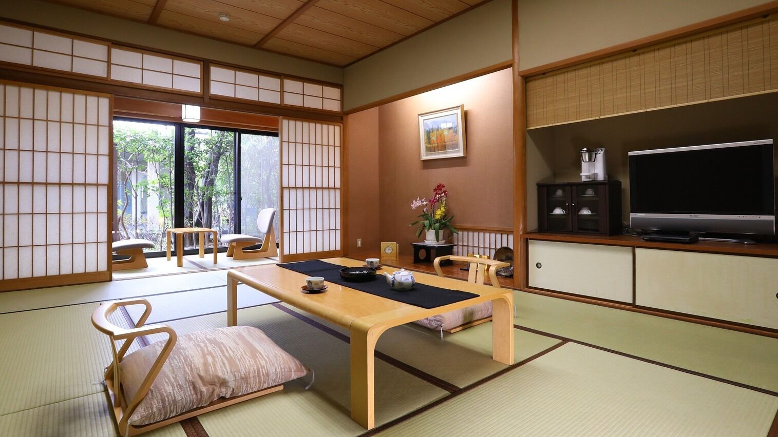 A traditional Japanese room with tatami flooring, a low table, a sofa, a TV, and a cabinet.