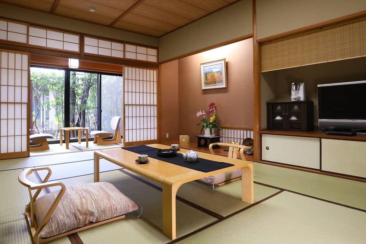 A traditional Japanese room with tatami flooring, a low table, a sofa, a TV, and a cabinet.