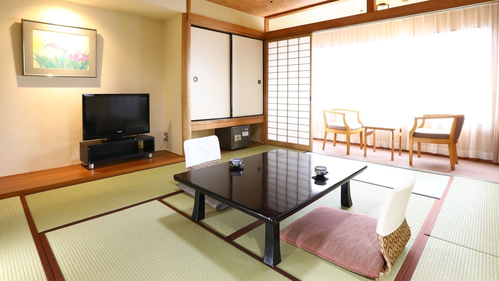 A traditional Japanese room with tatami flooring, a television, a sliding door, and a dining area with chairs.