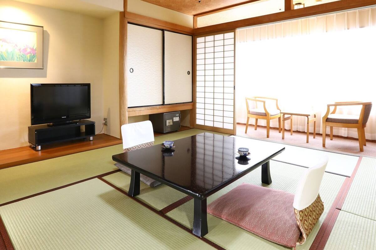A traditional Japanese room with tatami flooring, a television, a sliding door, and a dining area with chairs.