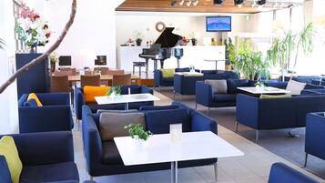 A modern lounge area with sofas, tables, and a piano.