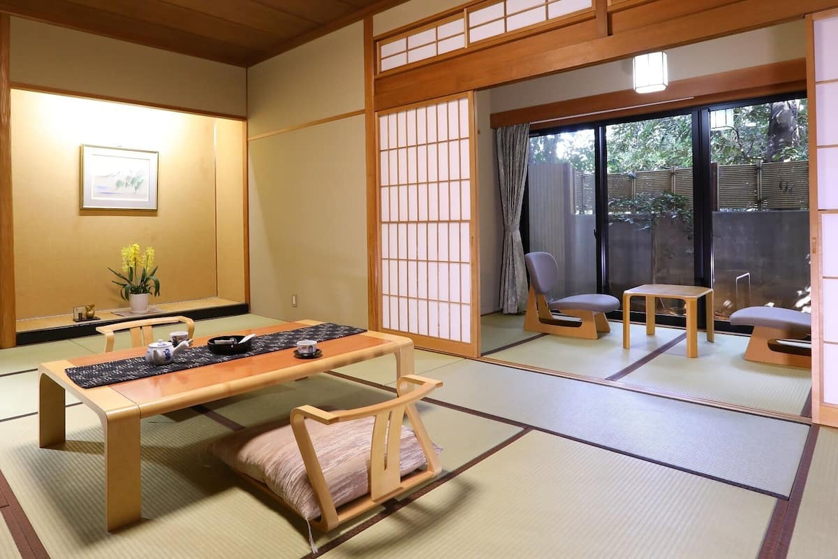 A traditional Japanese room with tatami flooring, a low table, a sofa, and a sliding door leading to a balcony.