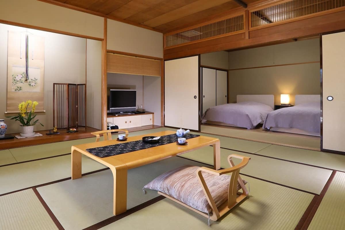 Une pièce de style japonais traditionnel, avec un sol recouvert de tatamis, une petite table avec un service à thé, un téléviseur et un lit avec une table de chevet.