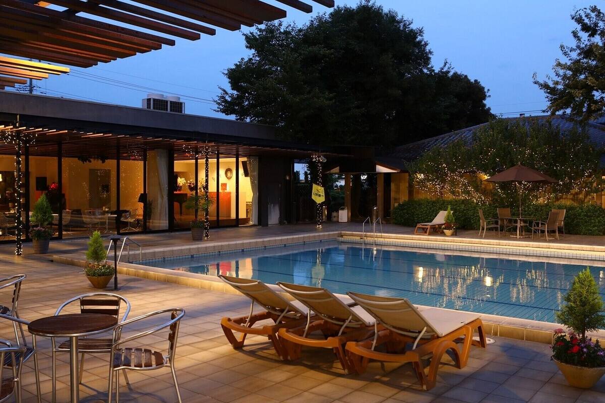 Un espace aménagé au bord de la piscine, avec des chaises longues, une table à manger et un restaurant doté de portes vitrées.