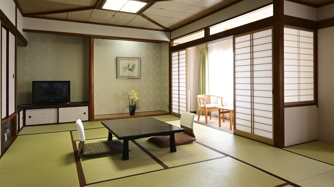 A traditional Japanese room with tatami flooring, a low table, a TV, a chair, and sliding doors.