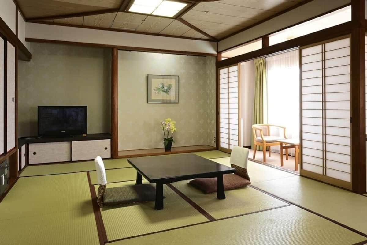 A traditional Japanese room with tatami flooring, a low table, a TV, a chair, and sliding doors.