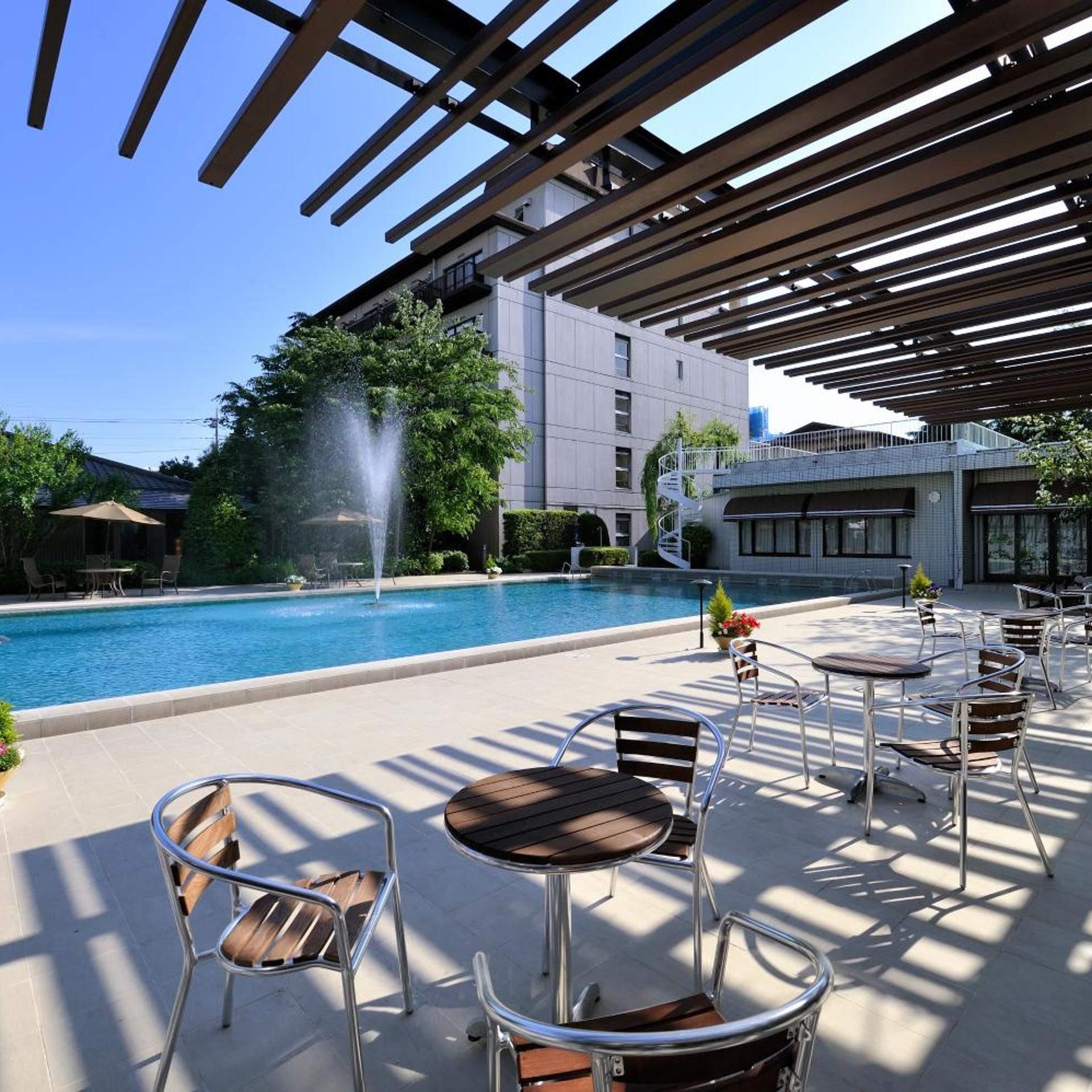 A poolside area with a fountain, outdoor seating, and a building in the background.