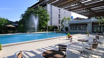 A poolside area with a fountain, outdoor seating, and a building in the background.