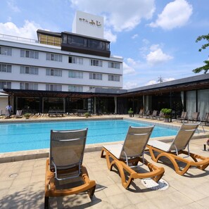 Un hôtel doté d’une piscine, de chaises longues et d’un espace extérieur aménagé avec des sièges, protégé par un auvent.