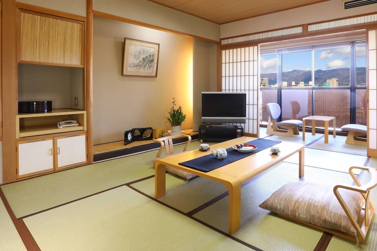 A traditional Japanese-style room with tatami flooring, a low table with a tea set, a television, and sliding doors leading to a balcony with a city view.