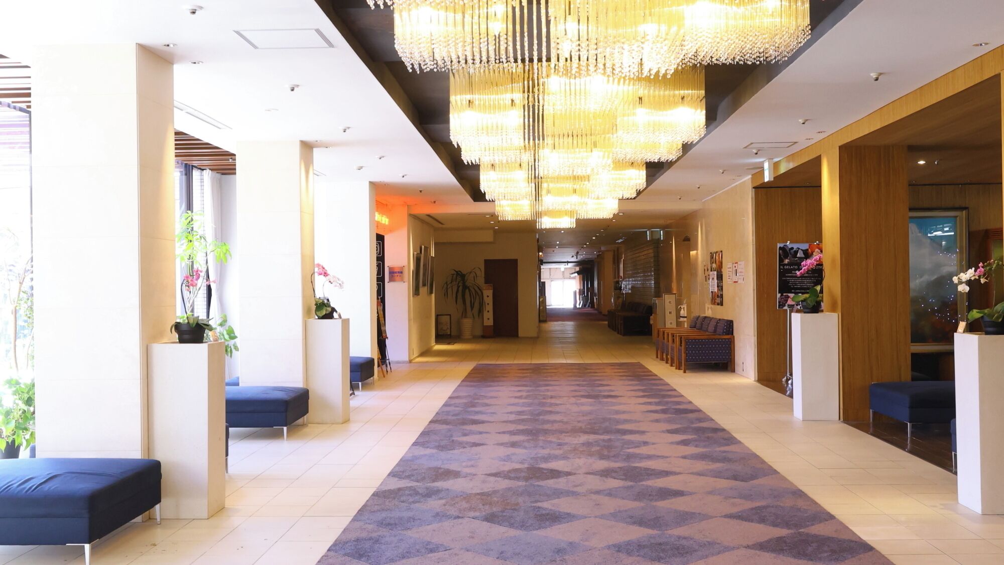 A hotel lobby with a central carpeted walkway, seating areas, and a large chandelier.