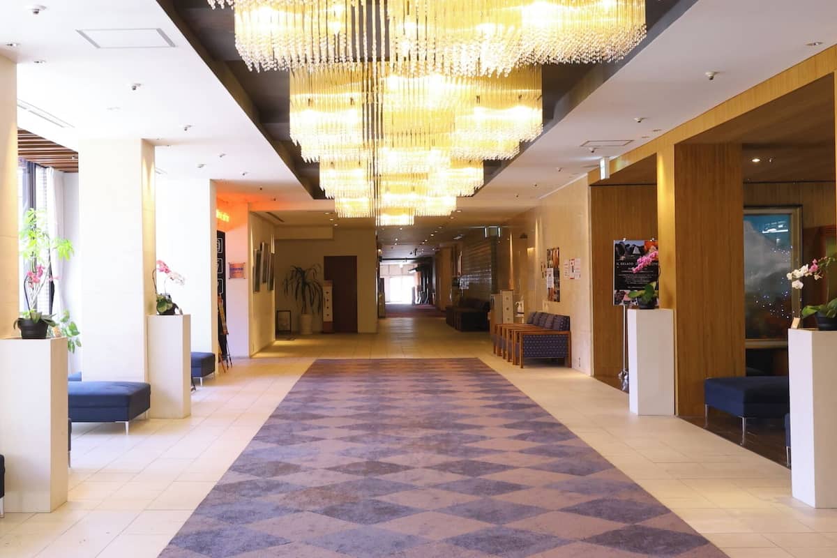A hotel lobby with a central carpeted walkway, seating areas, and a large chandelier.