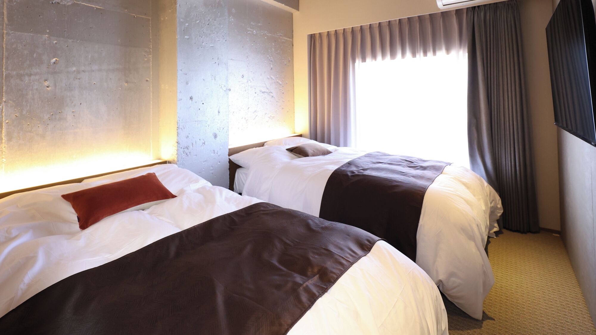 Two beds with white and brown bedding, a large window with curtains, and a wall with a textured surface.