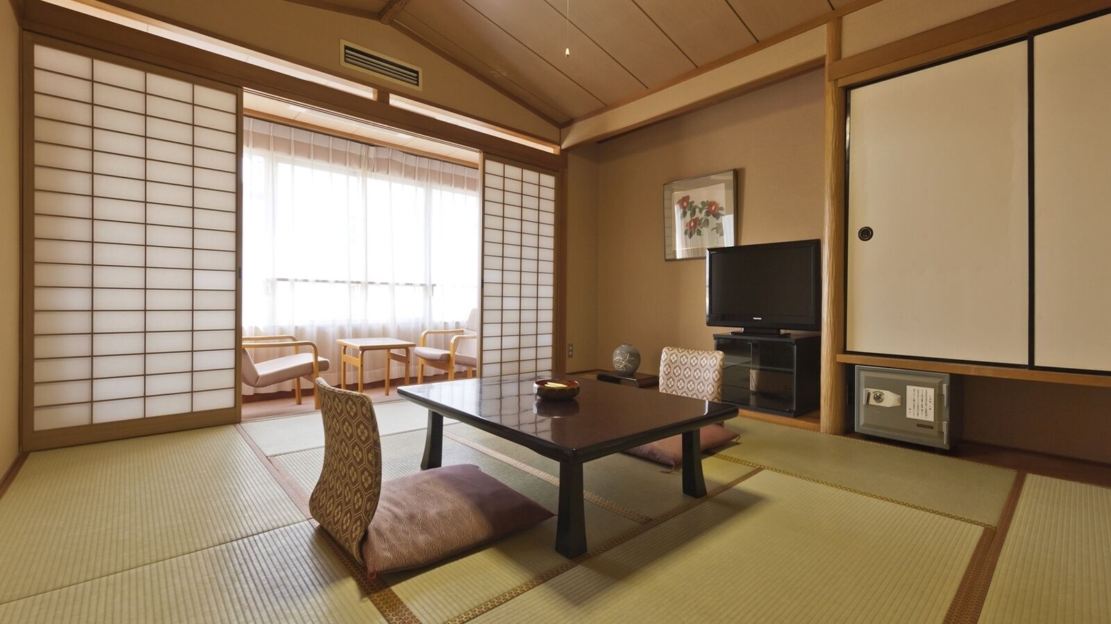 A traditional Japanese room with tatami flooring, a low table, chairs, a television, and sliding doors.