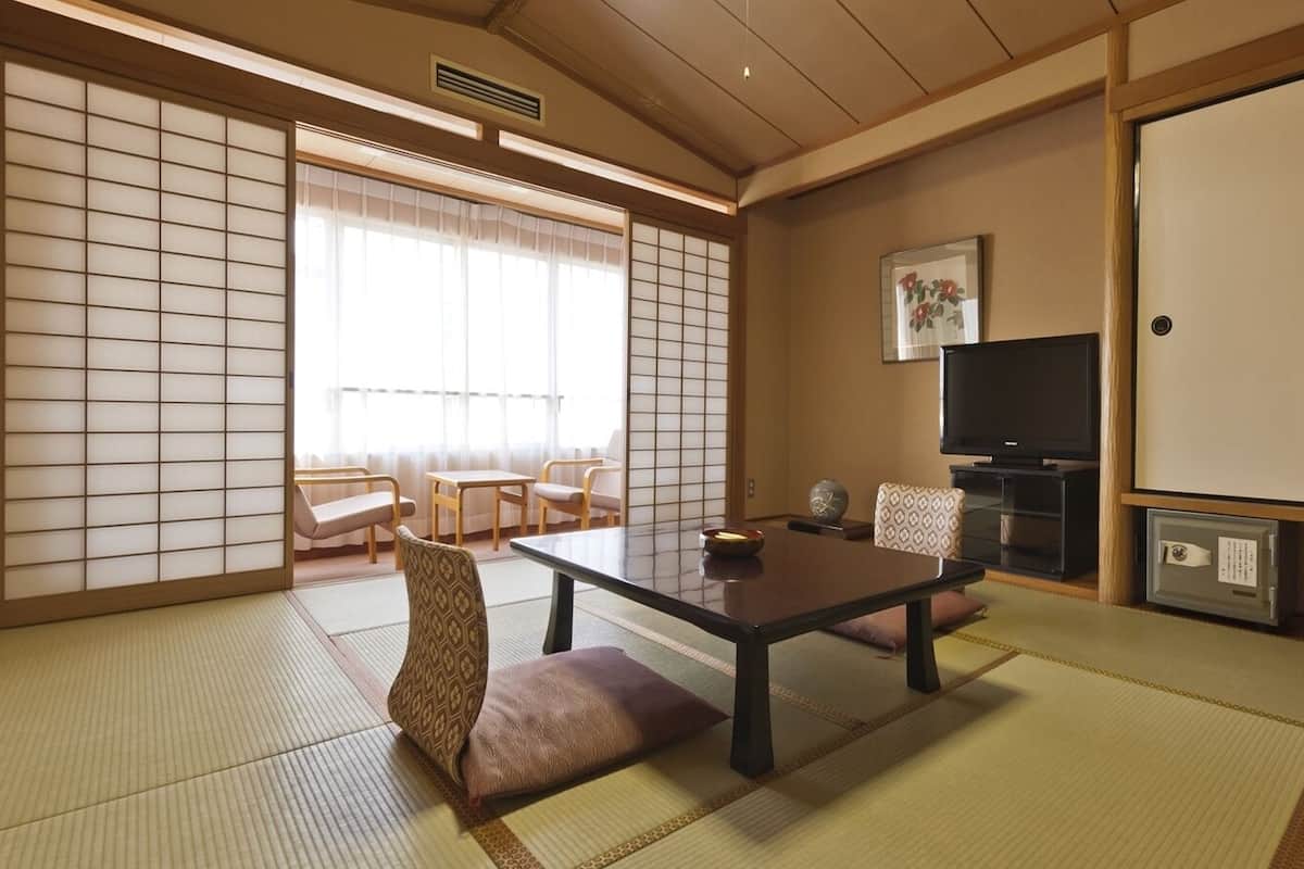 A traditional Japanese room with tatami flooring, a low table, chairs, a television, and sliding doors.