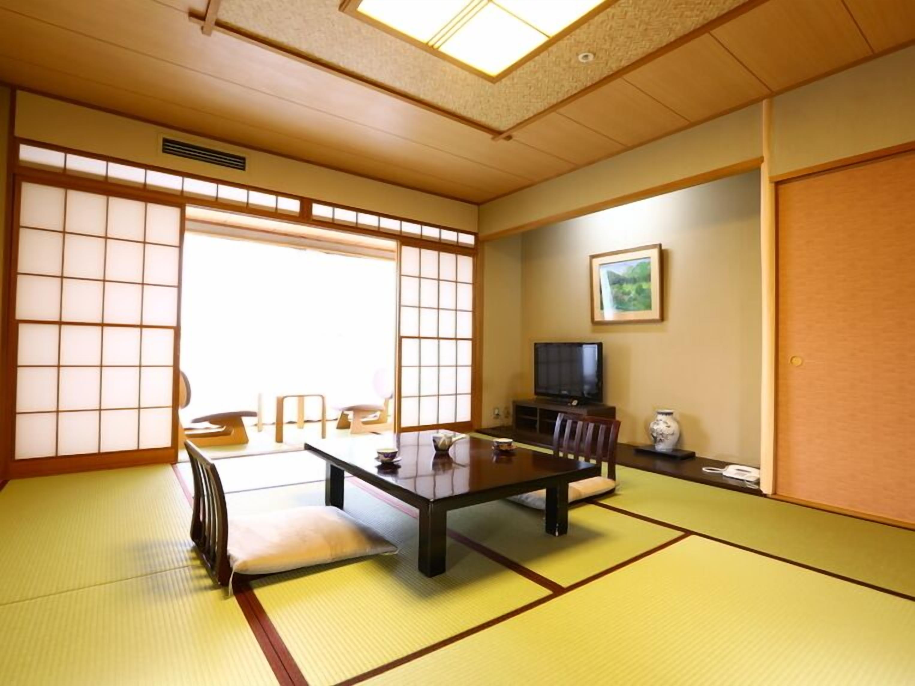 A traditional Japanese room with tatami flooring, a low table, a television, and sliding doors.