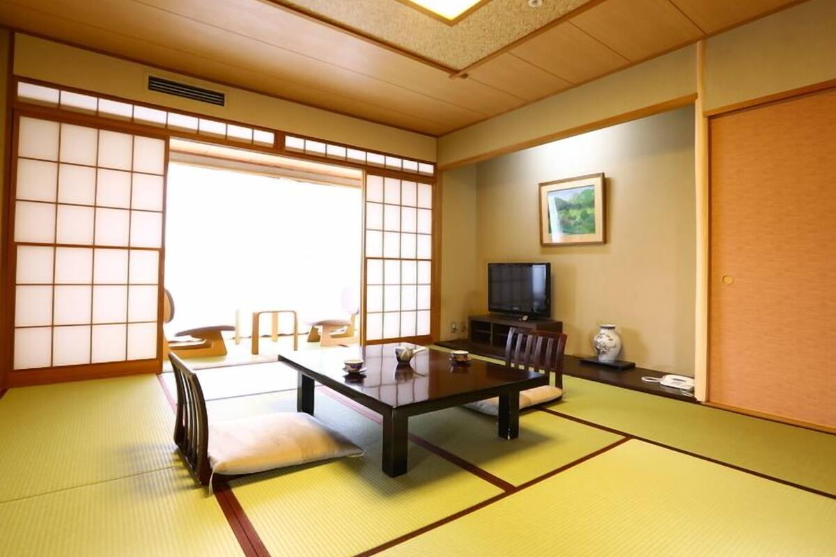 A traditional Japanese room with tatami flooring, a low table, a television, and sliding doors.