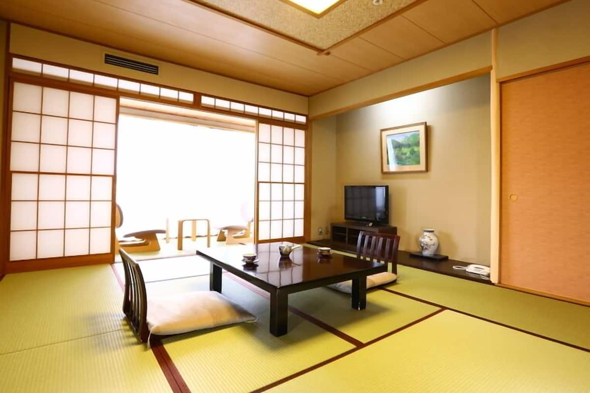 Une pièce de style japonais traditionnel, avec un sol recouvert de tatamis, une table basse, un téléviseur et des portes coulissantes.