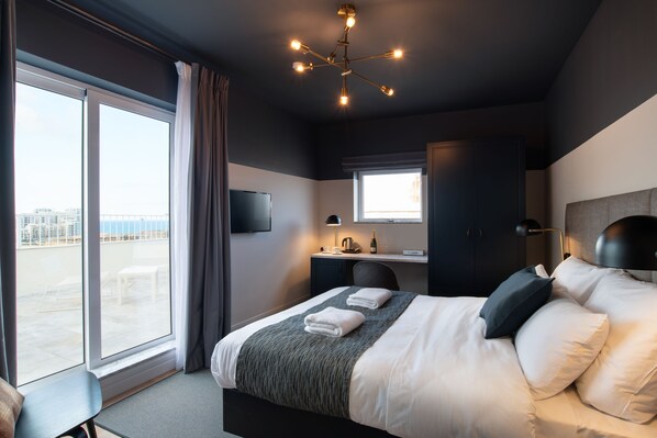 Habitación de hotel moderna con una cama grande, un escritorio, una silla y vistas de la ciudad a través de amplios ventanales.