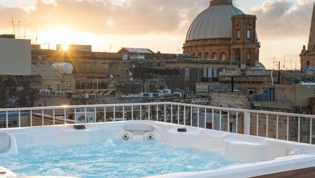 Een hottub met een houten buitenkant, met uitzicht op een stadsbeeld met historische gebouwen en een koepelconstructie.
