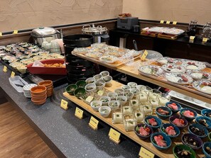 Un bufé con diversos platos y bebidas, incluyendo fuentes de comida, platos y una máquina de café.