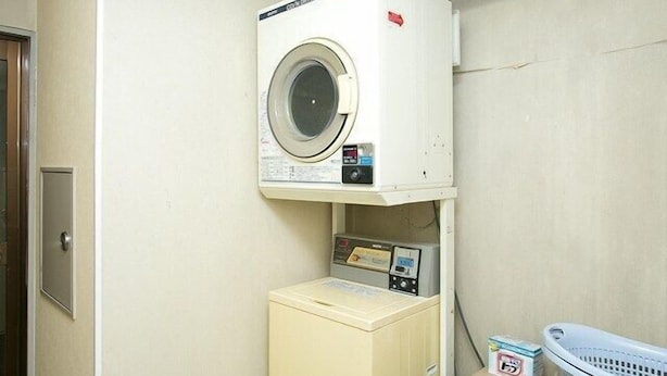 Een praktische wasruimte met een voorlader wasmachine en droger, een klein tafeltje met een mand, en een deur aan de linkerzijde.