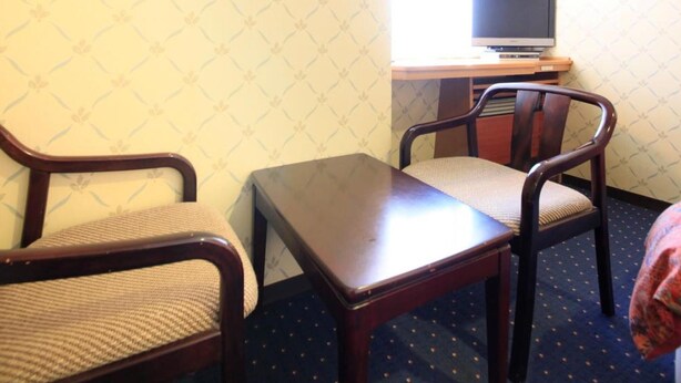 Hotellihuone, jossa on työpöytä, kaksi tuolia, televisio ja ikkuna, jossa on verhot.