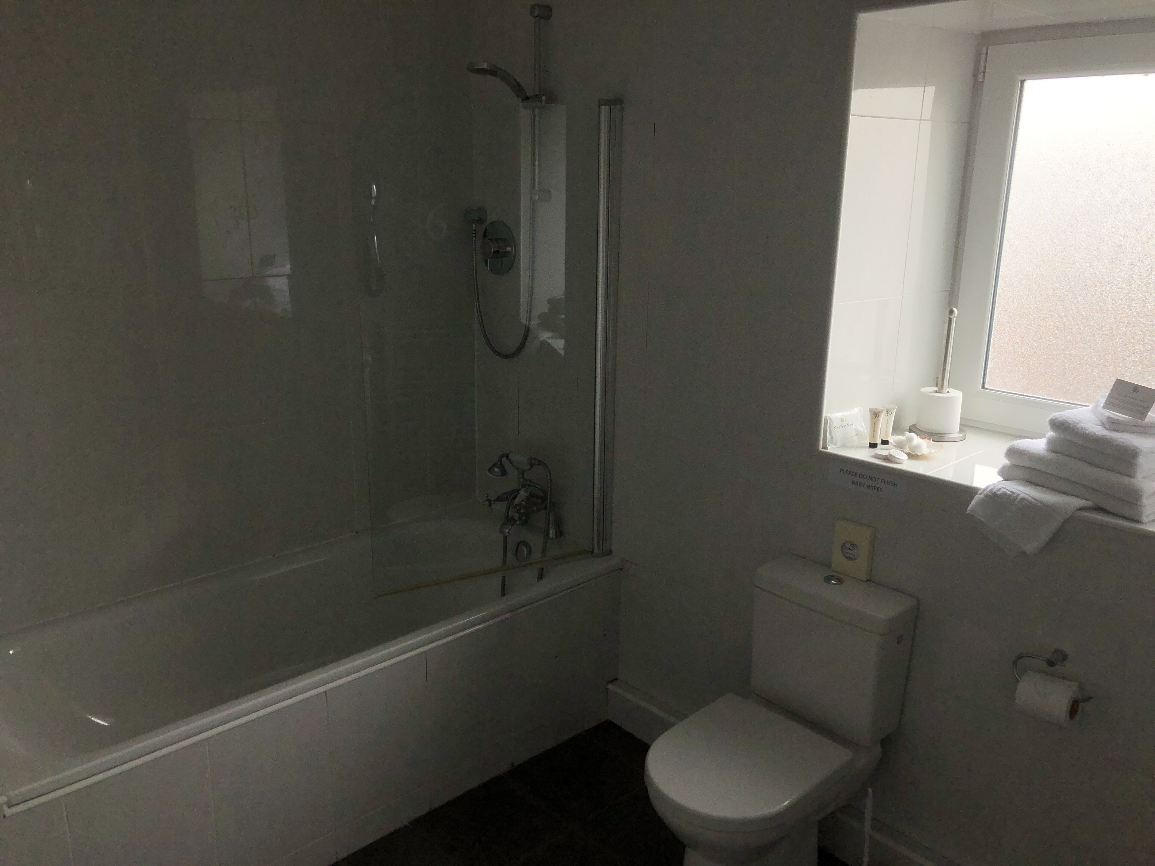 A bathroom with a bathtub, toilet, and a window with towels.